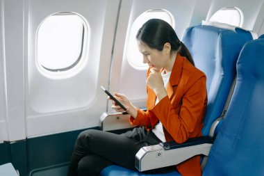 Resmi takım elbiseli Asyalı kadın yolcu akıllı telefon kullanarak rahat koltukta oturuyor. 