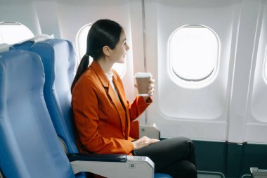 Resmi takım elbiseli, rahat koltukta oturan ve kahve içen Asyalı kadın yolcu. 