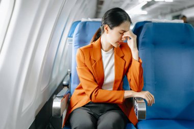 Hayal kırıklığına uğramış Asyalı kadın uçak yolcusu resmi bir takım elbise giymiş rahat koltukta oturuyor.
