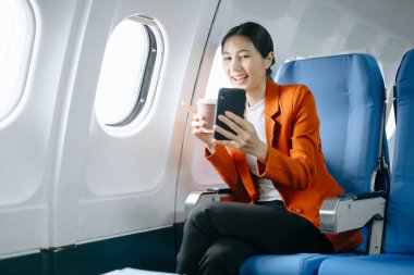 Resmi takım elbiseli Asyalı kadın yolcu rahat koltukta oturup kahve içerken görüntülü arama yapıyor. 