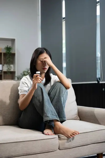 stock image frustrated asian woman take pills sitting on sofa at home 