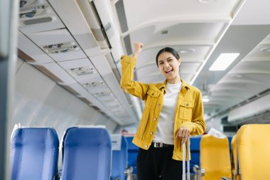 Çekici Asyalı kadın yolcu bavuluyla uçakta duruyor ve el kol hareketi yapıyor. 