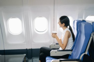 Çekici Asyalı kadın uçak yolcusu kahve içerken rahat koltukta oturuyor.