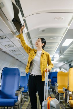 Çekici Asyalı kadın yolcu bavuluyla uçakta duruyor.