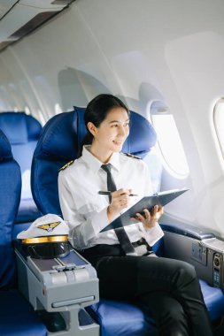 Asyalı, kendine güvenen, üniformalı kadın pilot, uçağın içinde oturuyor.