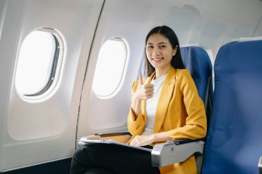 Genç Asyalı kadın uçakta oturuyor ve belgelerle çalışıyor. 