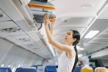 Çekici Asyalı kadın yolcu bavuluyla uçakta duruyor.