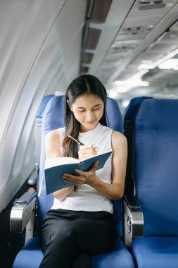 Resmi takım elbiseli Asyalı kadın yolcu rahat koltukta oturup notlar yazıyor. 