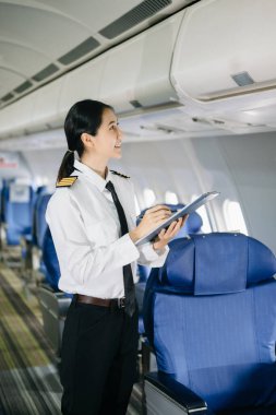 Asyalı, kendine güvenen, üniformalı kadın pilot, uçağın içinde poz veriyor.