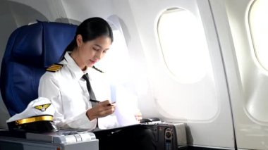 Asyalı, kendine güvenen, üniformalı kadın pilot, uçağın içinde oturuyor.