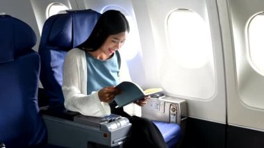 Çekici Asyalı kadın uçak yolcusu kitap okurken rahat koltukta oturuyor. Stil içinde seyahat et, zarafetle çalış.