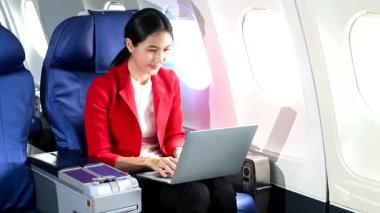 Resmi takım elbiseli Asyalı kadın yolcu rahat koltukta dizüstü bilgisayar kullanarak oturuyor. 