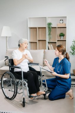 Doktor evdeki yaşlı hastayı muayene ediyor. Kadın terapist elinde pano tutuyor ve tekerlekli sandalyede oturan yaşlı bir kadınla ilgileniyor. Tıbbi servis kavramı