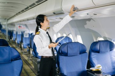 Asyalı, kendine güvenen, üniformalı kadın pilot, uçağın içinde poz veriyor.