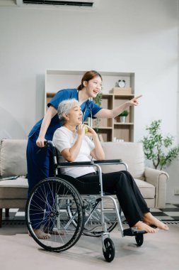 Hemşire el kol hareketi yapıyor ve evde elmalı yaşlı bir hasta var. Tekerlekli sandalyede oturan yaşlı kadınla ilgilenen terapist. Tıbbi servis kavramı  