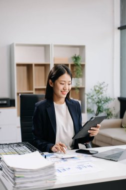 Genç ve güzel bir kadın çalışma yerinde otururken dizüstü bilgisayar ve dijital tablet kullanıyor. İşine odaklan..