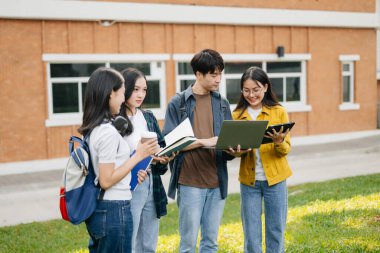 Genç Asyalı üniversite öğrencileri sabahleyin kampüs parkında ders çalışıyor. Birlikte vakit geçirmek, dizüstü bilgisayar ve dijital tablet kullanmak.
