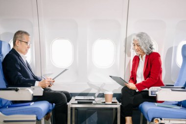 Uçakta iş toplantısı, Asyalı yetişkin işadamı ve iş kadını özel jetle uçuyor tablet ve laptop kullanarak belgeler üzerinde çalışıyorlar 