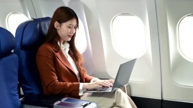 Resmi takım elbiseli Asyalı kadın yolcu rahat koltukta dizüstü bilgisayar kullanarak oturuyor. 