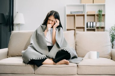 Kanepede battaniyeyle kaplanmış, grip belirtileri gösteren genç bir Asyalı kadın.. 