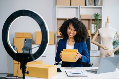 Mutlu Afro-Amerikan kadın blogcu video kaydediyor ya da dükkanında canlı yayında akıllı telefon kullanarak kıyafet satıyor. Çevrimiçi alışveriş konsepti 