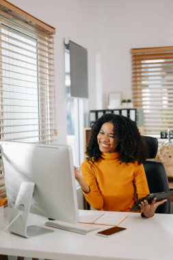 Mutlu Afro-Amerikan kadın ofiste tablet ve bilgisayar kullanarak çalışıyor.