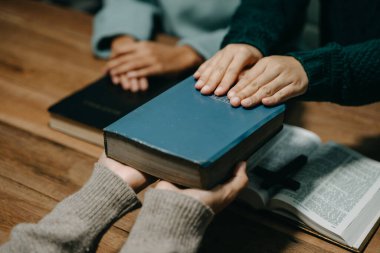 Bir grup Hıristiyan birlikte oturup ahşap bir masanın etrafında otururlar ve sınıfta bulanık incille dua ederler. Allah 'ın lütuf ve ihsanını dileyin..