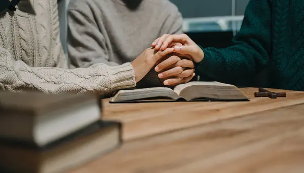 stock image Group of Christians sit together and pray around a wooden table with blurred Bible in homeroom. Prayer for brothers, faith, hope, and seek the blessings of God.