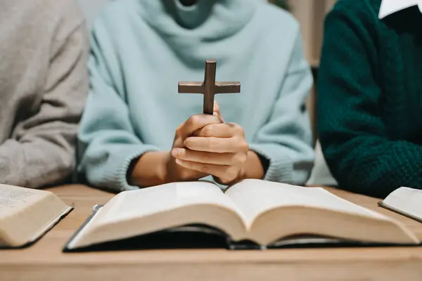 stock image Group of Christians sit together and pray around a wooden table with blurred Bible in homeroom. Prayer for brothers, faith, hope, and seek the blessings of God.