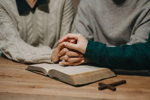 stock image Group of Christians sit together and pray around a wooden table with blurred Bible in homeroom. Prayer for brothers, faith, hope, and seek the blessings of God.