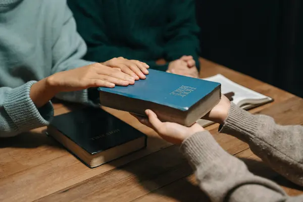 stock image Group of Christians sit together and pray around a wooden table with blurred Bible in homeroom. Prayer for brothers, faith, hope, and seek the blessings of God.