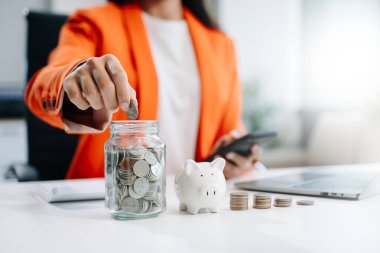 İş kadını cam kavanoza bozuk para koyar, akıllı telefon ve hesap makinesi kullanarak para hesaplar, tasarruf kavramı 