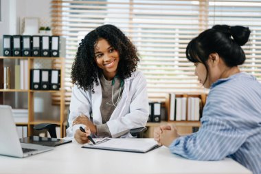 Ciddi Afrikalı Amerikalı kadın doktor harika haberler veriyor, hastanedeki Asyalı kadın hastayla sonuçları ya da belirtileri tartışıyor. 