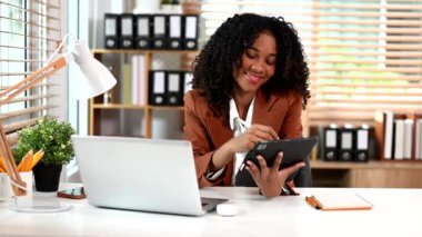 Genç Afrikalı Amerikalı iş kadını modern ofiste dizüstü bilgisayar ve dijital tablet üzerinde çalışıyor. 