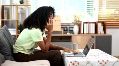 Genç bir kadın evdeki akıllı telefonunda dizüstü bilgisayar kullanarak rahat koltukta dinleniyor.