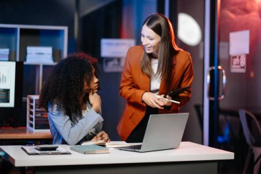 Modern ofisteki dizüstü bilgisayarları kullanarak bir proje üzerinde çalışan iki farklı kadın.