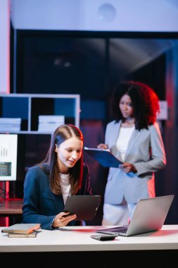 Modern ofiste tablet ve laptop kullanan iki farklı kadın bir projede birlikte çalışıyor. İş çözümlerini, planları, fikirleri tartışıyorlar.