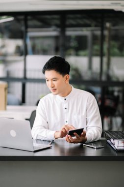 Modern ofisteki ahşap masada oturan yakışıklı genç adam.