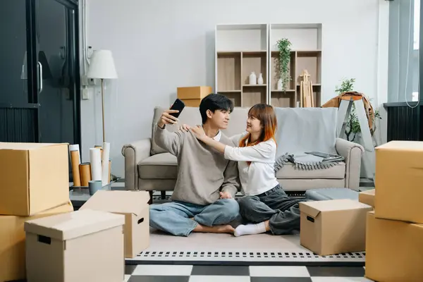 stock image Happy asian young attractive couple man and woman with big boxes moving into a new house and taking selfie on smartphone 