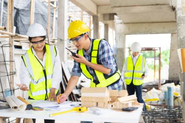 Mimar Asyalı takım inşaat alanında iş arkadaşlarıyla birlikte çalışıyor. Büyük projede mimarlık mühendisliği. İnşaat sürecinde bina içi.