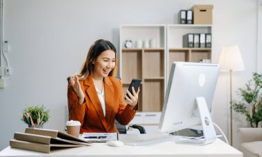 Genç, pozitif kadın muhasebeci bilgisayarını ve telefonunu kullanarak ekiple konuşuyor.