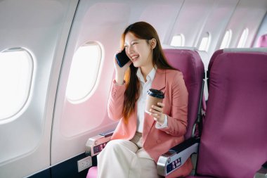 Pembe ceketli, başarılı bir Asyalı iş kadınının portresi. Uçakta birinci sınıfta oturmuş telefonla konuşuyor ve kahve içiyor. 