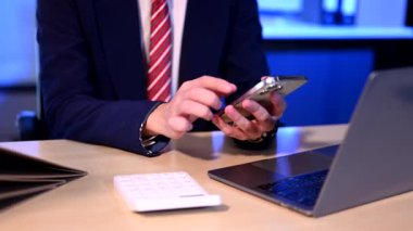 Genç iş adamı ofiste fazla mesai yapıyor, akıllı telefon, dizüstü bilgisayar kullanıyor ve proje yapıyor. 