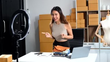 Küçük işletme girişimcisi KOBİ serbest. Ev ofisinde çalışan Asyalı bir kadın sosyal medya için paketleme ve akıllı telefon ve yüzük lambası kullanıyor.