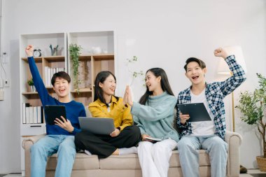 Dijital tabletli dizüstü bilgisayar ve evde online bilgi kullanarak proje ödevi üzerinde çalışan bir grup Asyalı genç üniversite öğrencisi 