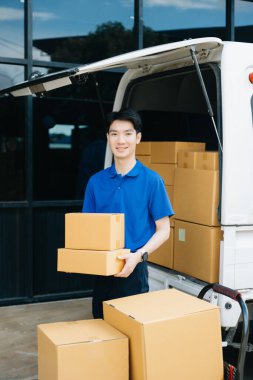 Ambarın dışında minibüsün yanında duran Asyalı kurye portresi. Burası bir nakliye ve dağıtım deposu.. 