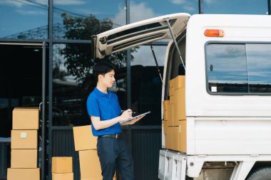 Ambarın dışında minibüsün yanında duran Asyalı kurye portresi. Burası bir nakliye ve dağıtım deposu.. 