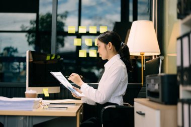 Asyalı iş kadını geceleri modern ofiste bilgisayarda çalışıyor.  