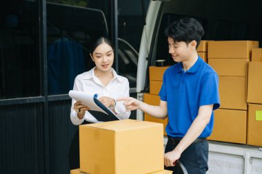 Express Teslimat Servisi. Asyalı kurye bayan müşteriye paket teslim ediyor. Deponun dışında kargo servisi, eve teslimat ve nakliye konsepti.