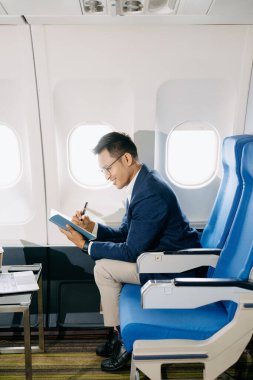 Çekici bir Asyalı işadamının uçak koltuğunda ajandasına notlar yazışının yan görüntüsü